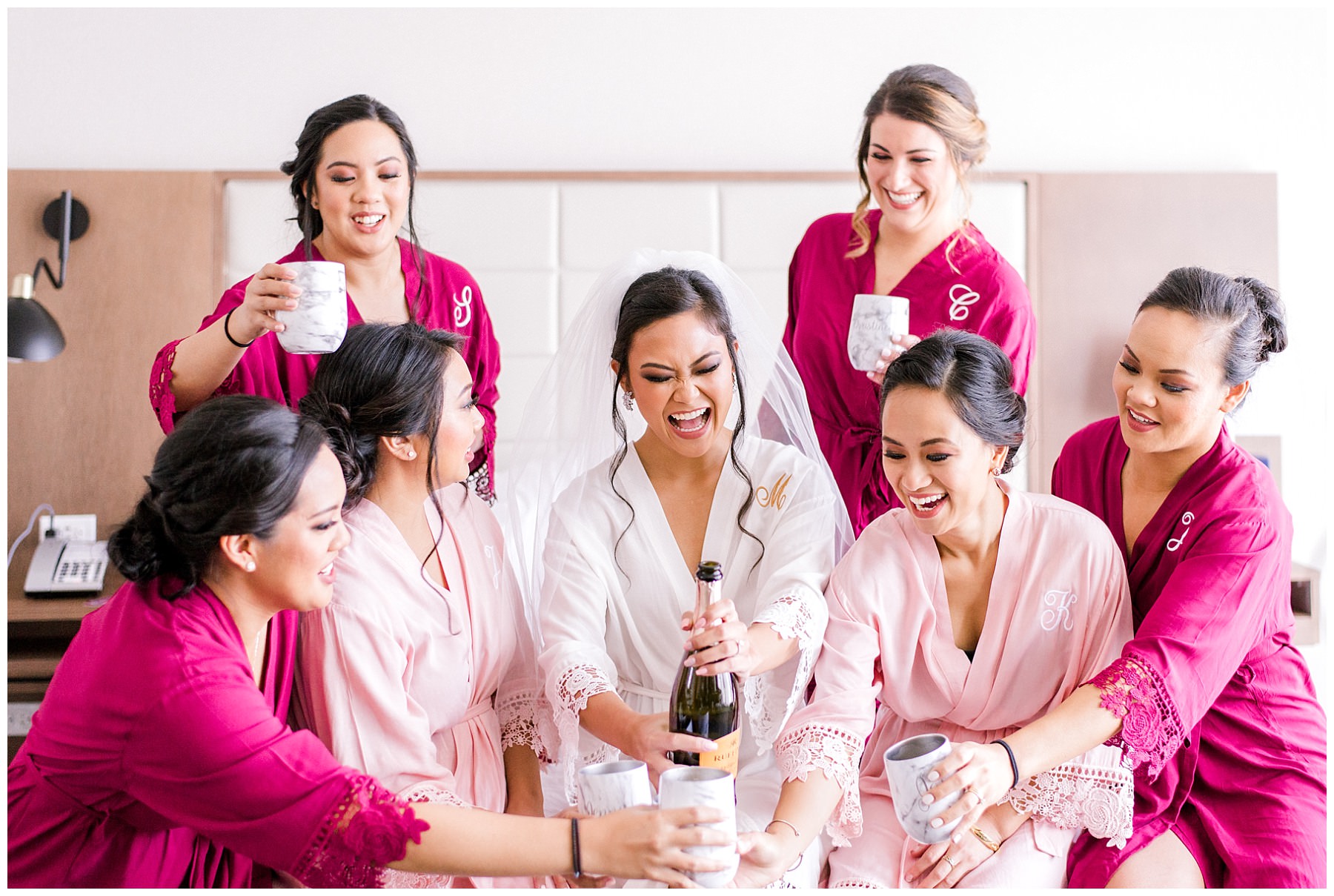 bride popping a champagne with her bridesmaids while sitting on a bed 