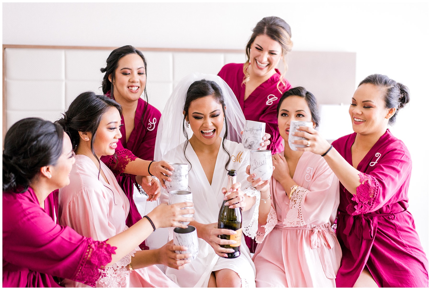 bride popping a champagne with her bridesmaids while sitting on a bed