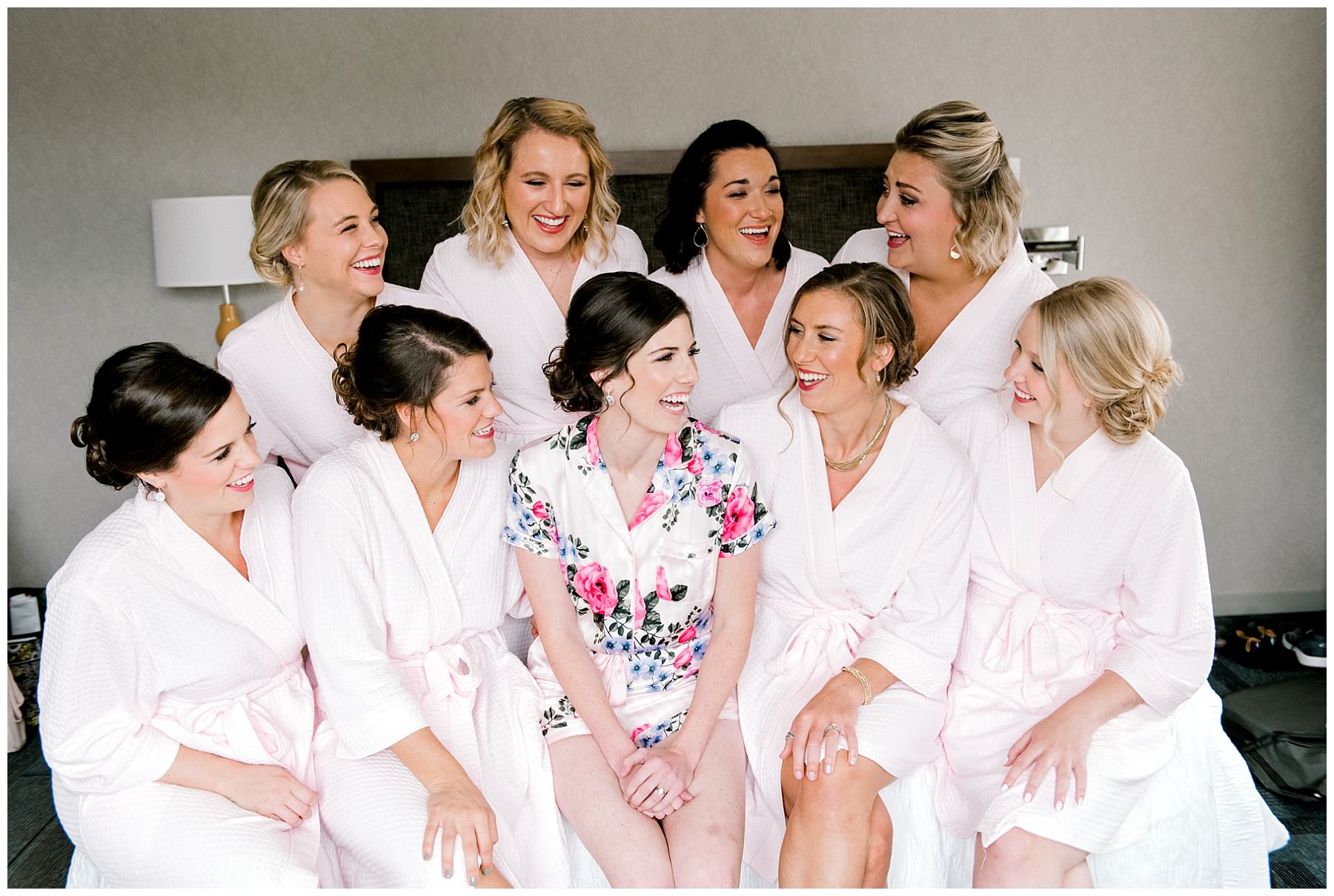 bride and bridesmaids with matching outfits sitting on a bed and laughing
